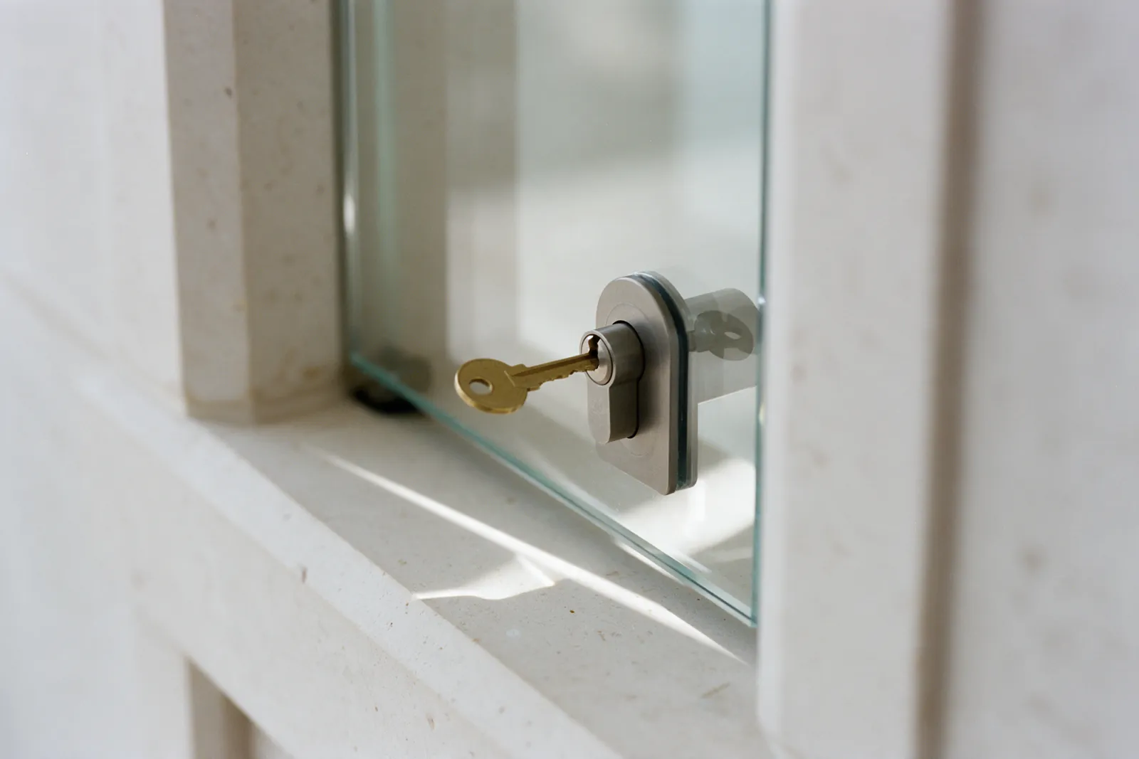 A key in the lock of a glass door set in a limestone frame, in morning light.