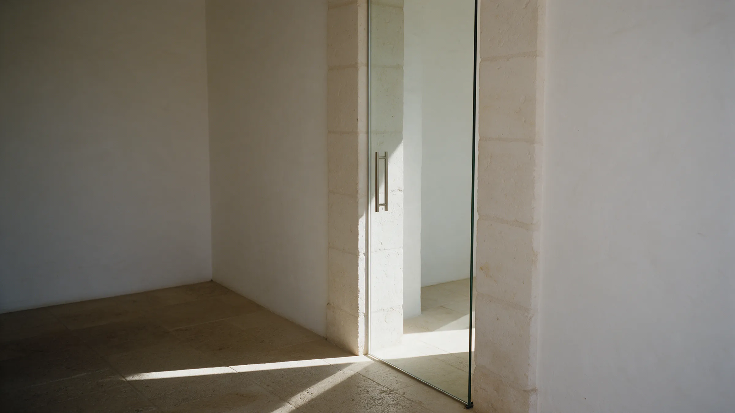 A glass door in a limestone wall, left slightly open; a blade of light passes through the gap onto the floor.